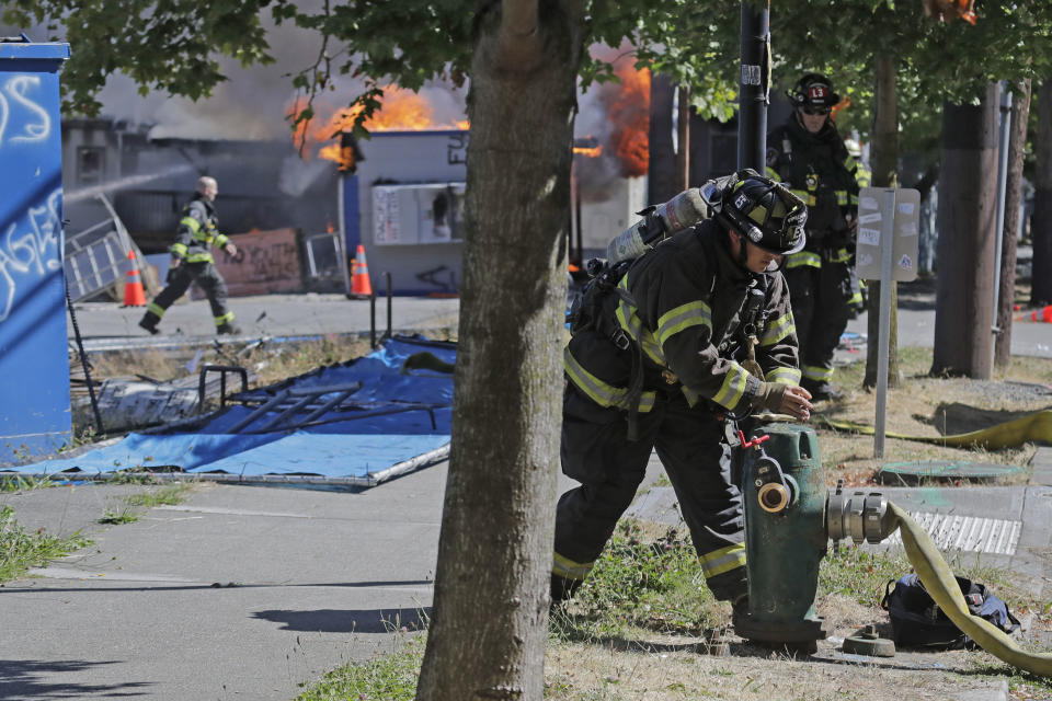 A firefighter turns on a hydrant as construction buildings burn near the King County Juvenile Detention Center, Saturday, July 25, 2020, in Seattle, shortly after protesters left the area. A large group of protesters were marching Saturday in Seattle in support of Black Lives Matter and against police brutality and racial injustice. Protesters broke windows and vandalized cars at the facility. (AP Photo/Ted S. Warren)