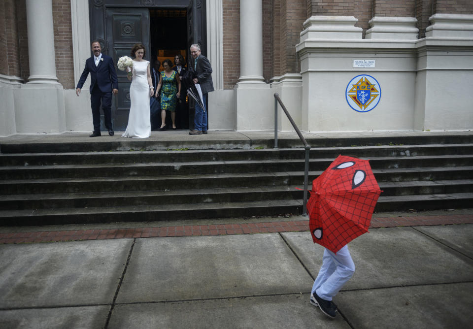 As the ring bearer walks by with an umbrella, newlyweds Associated Press photographer Gerald Herbert, back left, and Lucy Sikes walk out of Mater Dolorosa Catholic Church in New Orleans, Friday, July 12, 2019. Originally scheduled for Saturday, the couple moved their nuptials up a day to avoid the arrival of Tropical Storm Barry. (Max Becherer/The Advocate via AP)