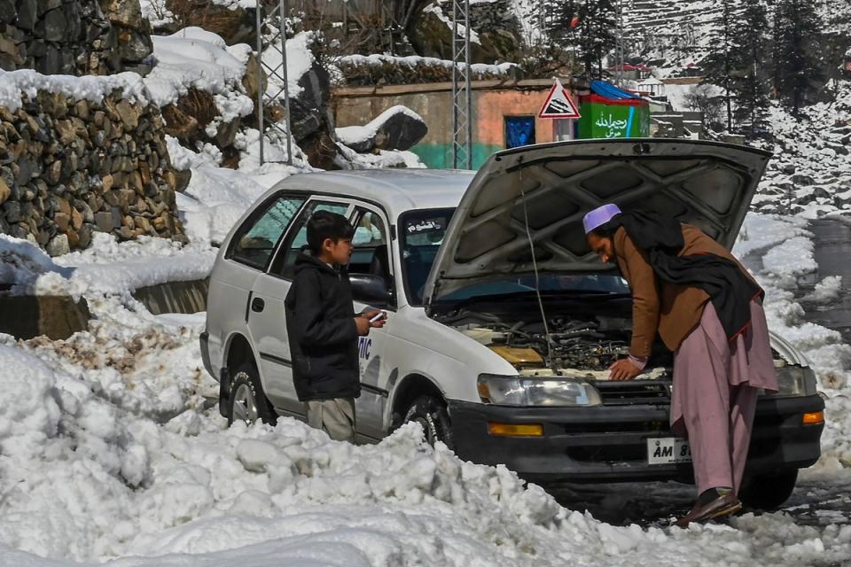 A man fixes his car along a snow laden street in Kalam on 4 March 2024 (AFP via Getty Images)