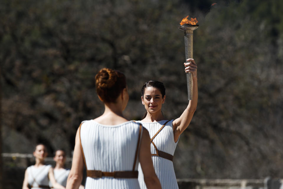 Greek actress Xanthi Georgiou, playing the role of the High Priestess, holds up the torch during the flame lighting ceremony at the closed Ancient Olympia site, birthplace of the ancient Olympics in southern Greece, Thursday, March 12, 2020. Greek Olympic officials are holding a pared-down flame-lighting ceremony for the Tokyo Games due to concerns over the spread of the coronavirus. Both Wednesday's dress rehearsal and Thursday's lighting ceremony are closed to the public, while organizers have slashed the number of officials from the International Olympic Committee and the Tokyo Organizing Committee, as well as journalists at the flame-lighting. (AP Photo/Thanassis Stavrakis)
