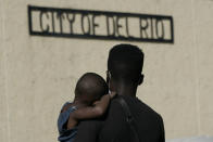 A Haitian migrant carries a boy while waiting to board a bus provided by a humanitarian group after being released from U.S. Customs and Border Protection custody, Friday, Sept. 24, 2021, in Del Rio, Texas. The “amistad,” or friendship, that Del Rio, Texas, and Ciudad Acuña, Mexico, celebrate with a festival each year has been important in helping them deal with the challenges from a migrant camp that shut down the border bridge between the two communities for more than a week. Federal officials announced the border crossing would reopen to passenger traffic late Saturday afternoon and to cargo traffic on Monday. (AP Photo/Julio Cortez)