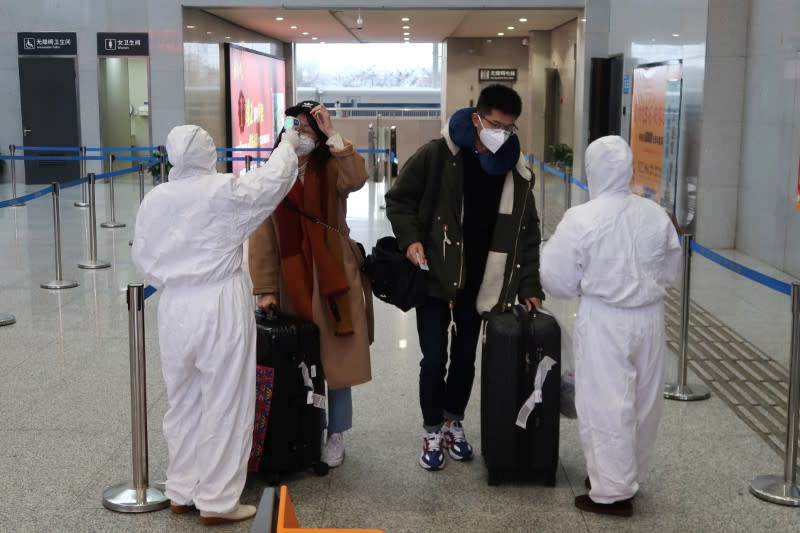 Workers in protective suits check the temperature of passengers arriving at the Xianning North Station on the eve of the Chinese Lunar New Year celebrations, in Xianning