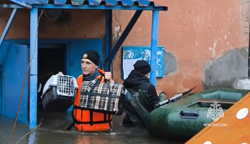 In this grab taken from a video released by the Russian Emergency Ministry Press Service on Sunday, April 7, 2024, an emergency worker carries belongings of people during an evacuation of local residents after part of a dam burst causing flooding, in Orsk, Russia. State media say Russia's government has declared the situation in flood-hit areas in the Orenburg region a federal emergency. The floods, caused by rising water levels in the Ural River, forced over 4,000 people, including over 800 children, to evacuate, the regional government said. (Russian Emergency Ministry Press Service via AP)