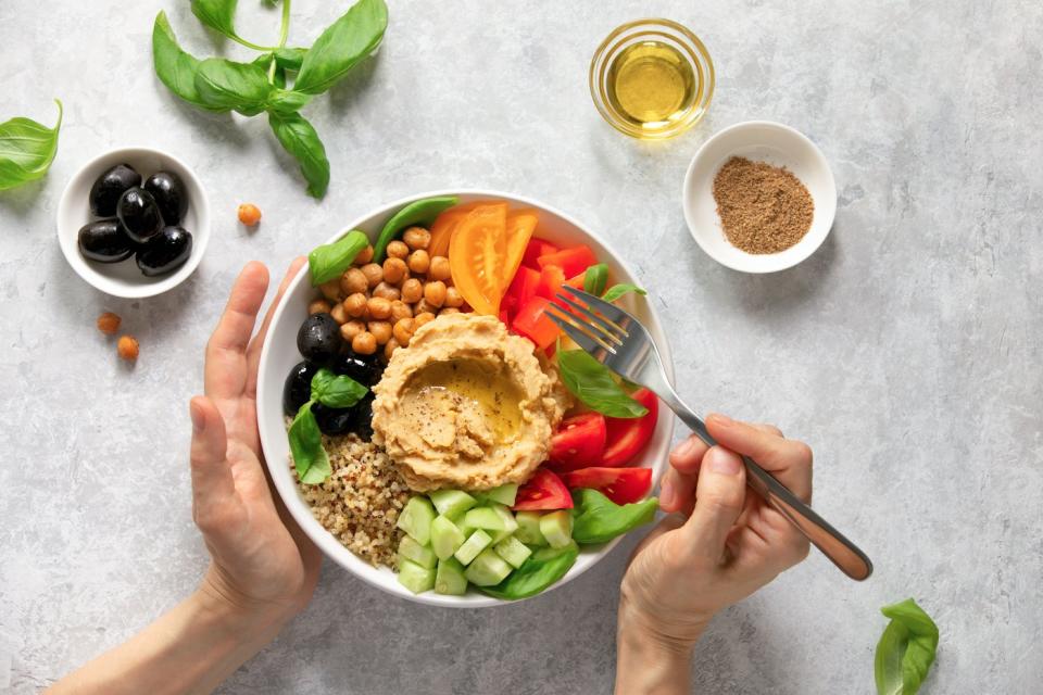 Hands holding a bowl of Mediterranean food. 