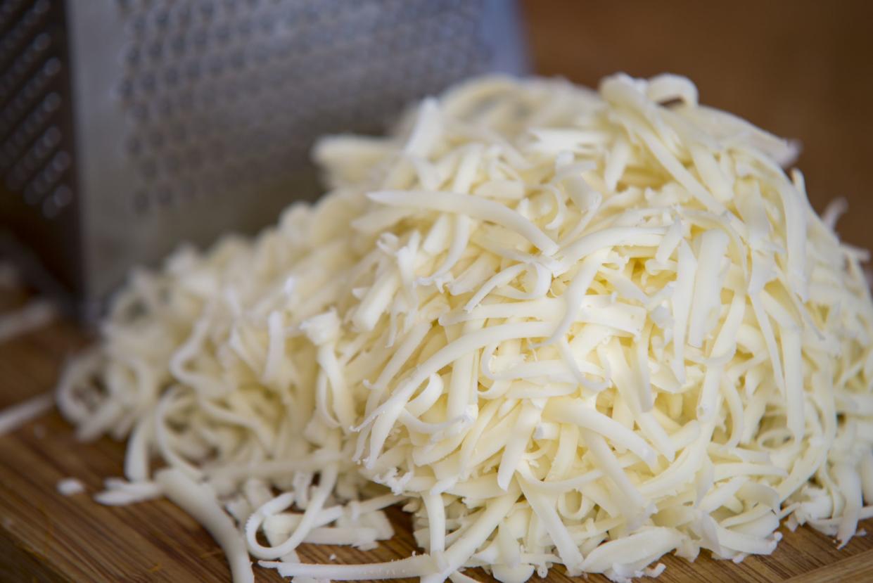 Shredded mozzarella cheese on a cutting board with a grater