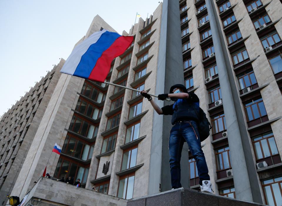 Pro-Russian masked activist waves a Russian national flag in front of the regional administration building in Donetsk, Ukraine, Sunday, April 6, 2014. In Donetsk a large group of people surged into the provincial government building and smashed windows. A gathering of several hundred, many of them waving Russian flags, then listened to speeches delivered from a balcony emblazoned with a banner reading a "Donetsk Republic". (AP Photo/Andrey Basevich)