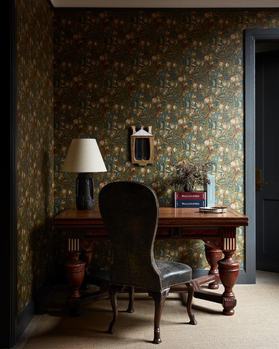 a desk with a lamp and a chair in front of a wall with art