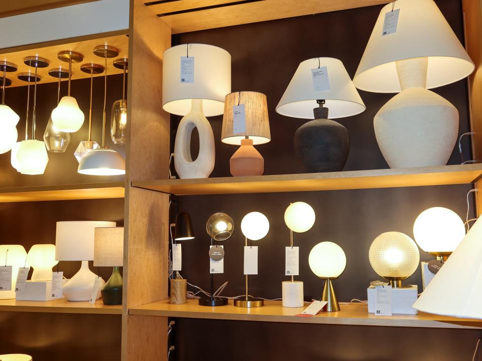 A wooden shelf with several lamps at West Elm. The lamps are black, metal, brown, and white.