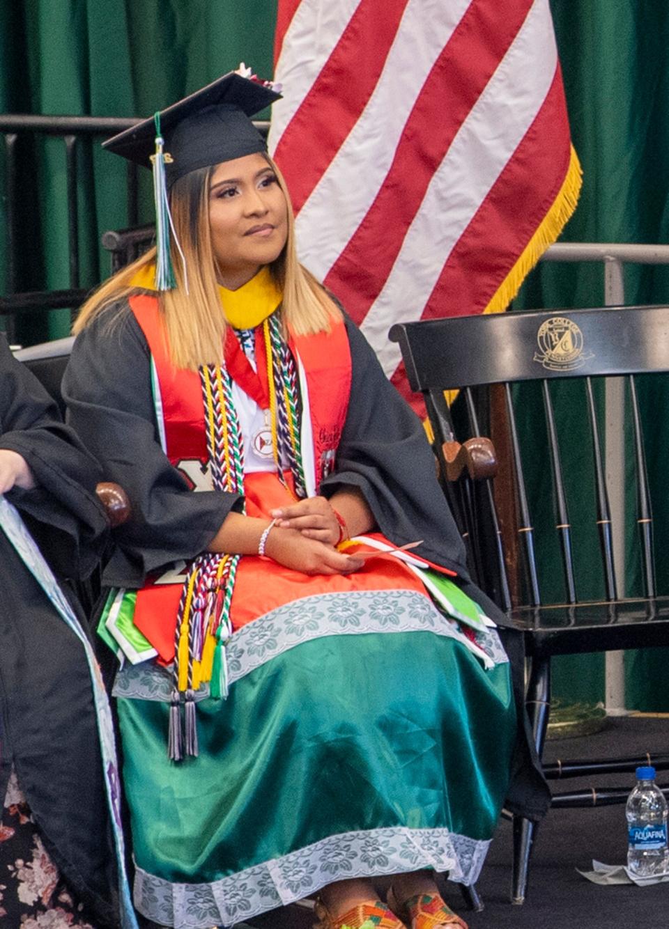 Jenifer Hernandez-Vargas listens to speakers from the platform after delivering her student remarks. During the speech, she opened her graduation gown to reveal a replica of a dress she was wearing the day she left Mexico. That was a symbolic moment for her that, in retrospect, guided her to a better future.