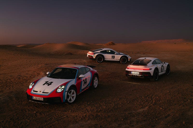 Three Porsche 911 Dakars are parked on sand, each in a different historic rally livery.