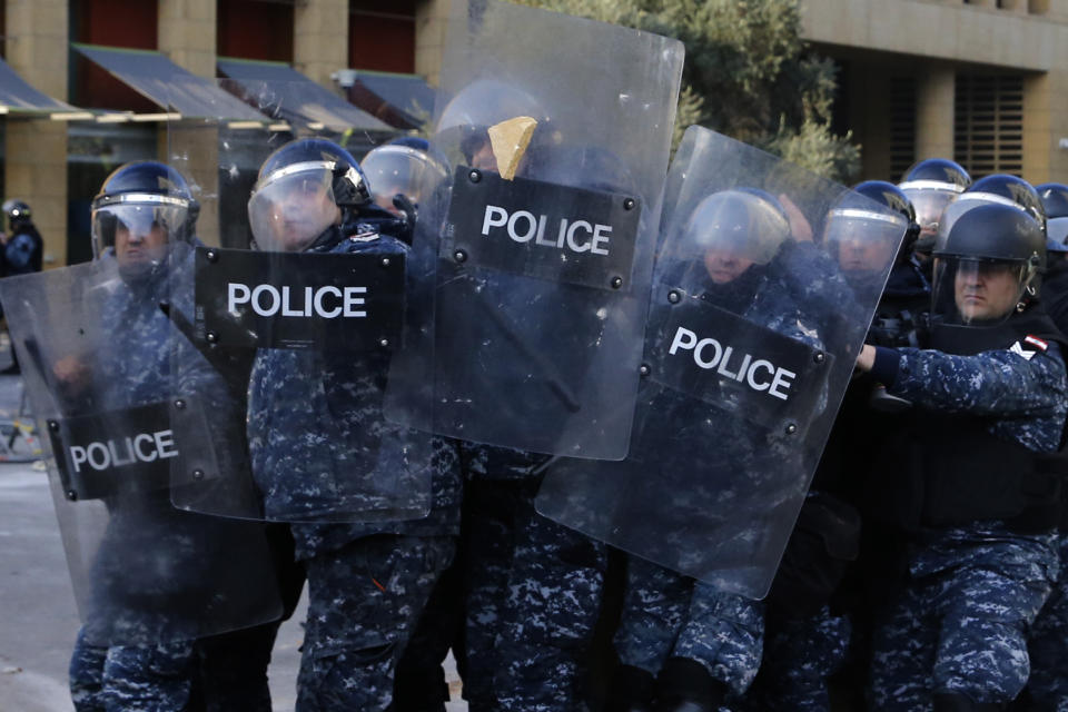 Riot police shield themselves from stones thrown by protesters during a protest against a parliament session holding a vote of confidence for the new government in downtown Beirut, Lebanon, Tuesday, Feb. 11, 2020. (AP Photo/Bilal Hussein)