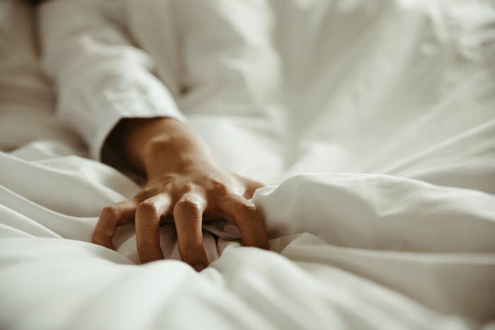 Close-up of a person's hand gripping bedsheets, suggesting intimacy