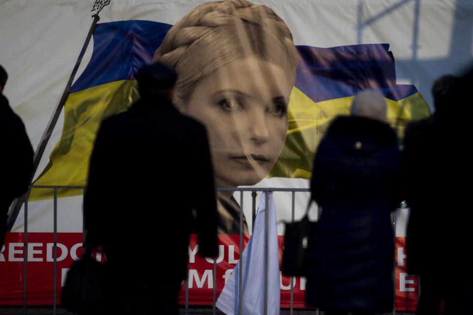 People pass by a portrait of Yulia Tymoshenko, a prominent opposition leader at Independence Square in Kiev, Ukraine, Monday, Feb. 24, 2014. Ukraine's acting government issued a warrant Monday for the arrest of President Viktor Yanukovych, last reportedly seen in the pro-Russian Black Sea peninsula of Crimea, accusing him of mass crimes against protesters who stood up for months against his rule. (AP Photo/Marko Drobnjakovic)