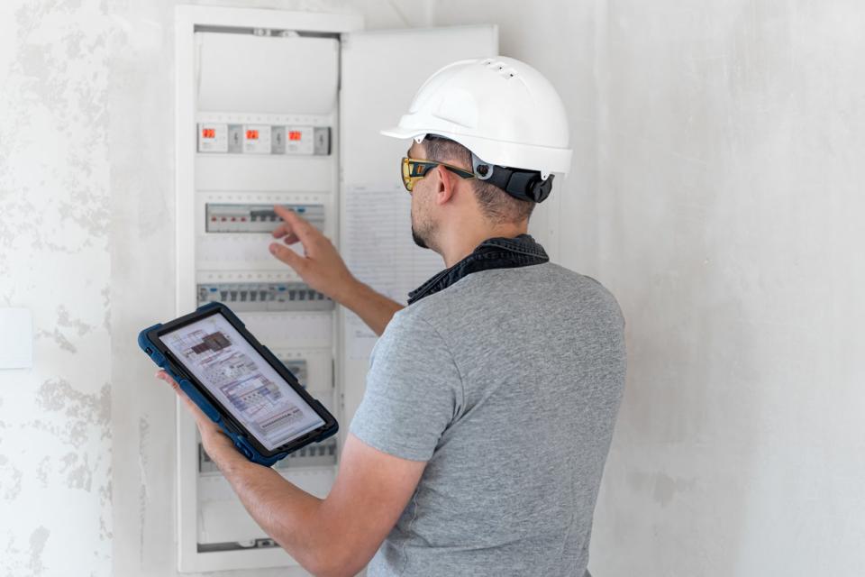 Energy inspector in hardhat examines home switchboard.