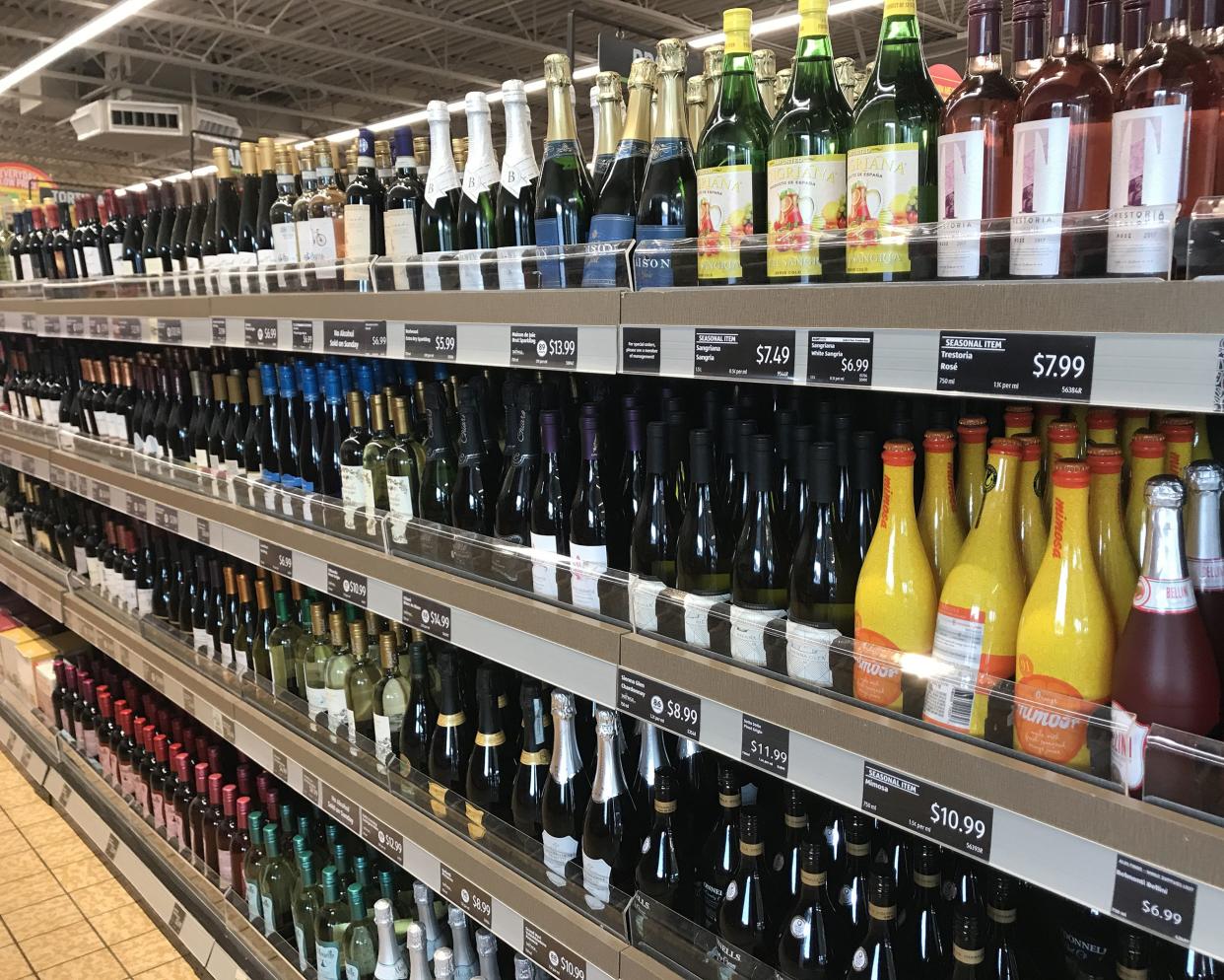 One side of an aisle 4 rows of wine and champagnes in an Aldi store, organized with descriptions and prices underneath, tile floor on the bottom left side