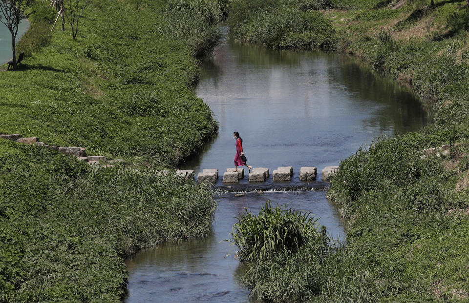 A woman wearing a face mask to help protect against the spread of the new coronavirus crosses a stream in Seoul, South Korea, Wednesday, July 15, 2020. (AP Photo/Lee Jin-man)