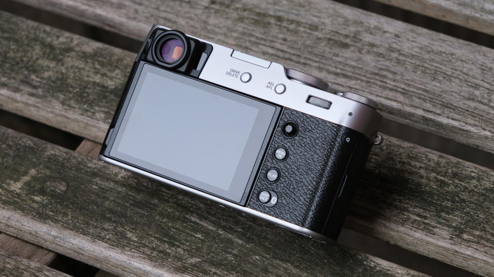 Fujifilm X100VI camera showing the screen and buttons, sat on on a slatted wooden bench