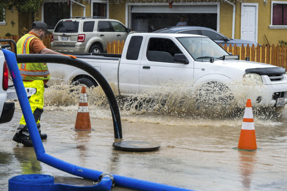 A member of public works clears a flooded storm drain on E Bolivar Street in Salinas, Calif., Tuesday, Dec. 27, 2022. The first in a week of storms brought gusty winds, rain and snow to California on Tuesday, starting in the north and spreading southward.(AP Photo/Nic Coury)