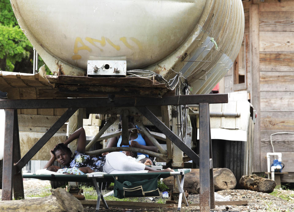 Women and children rest under a water tank at a migrant camp in Lajas Blancas, Darien province, Panama, Saturday, Aug. 29, 2020. The flow of migrants through the dense and dangerous Darien jungle has been going strong for more than a decade. This is the first time authorities have stopped it because of the ongoing new coronavirus pandemic. (AP Photo/Arnulfo Franco)