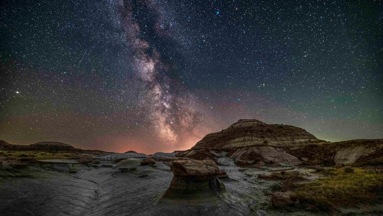  The summer Milky Way and galactic core region over the formations at Dinosaur Provincial Park, Alberta, July 9, 2021, on a warm moonless night. This is a blend of 4 tracked exposures (2 to 3 minutes each) at f/2.8 for the sky and 3 untracked exposures (4 to 8 minutes) at f/5.6 for the foreground. An additional tracked exposure through a Kase/Alyn Wallace Starglow filter adds some subtle glows to the bright stars. Two of the sky exposures were shot through a Kase Natural Night filter as a test, but it didn't make a big difference over the unfiltered images. All with the Canon Ra at ISO 1600 to 3200, and on the Star Adventurer 2i tracker, and with the Canon 15-35mm RF lens. No artificial lighting was employed here. Smoke from BC forest fires spoiled the transparency and contrast in the sky. (Photo by: Alan Dyer/VW Pics/Universal Images Group via Getty Images) 