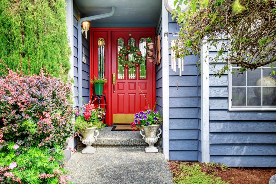 House with blue siding, a red front door, and cottage-type flowers around a paved walkway.