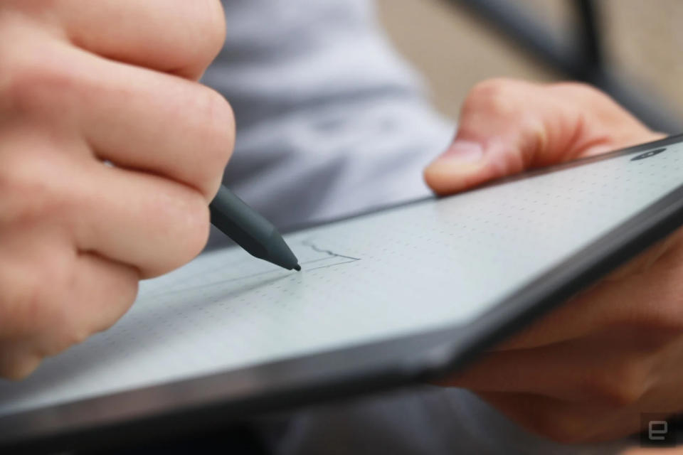 A person writing with a stylus on the Kindle Scribe e-reader / digital notebook. The photo is taken from the side.