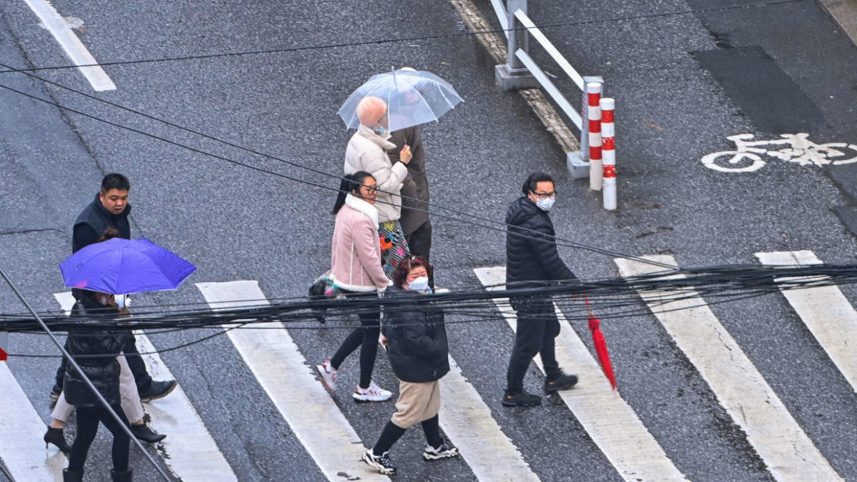 People walk on a street in the Jing'an district in Shanghai on December 3, 2022. (Photo by Hector RETAMAL / AFP)