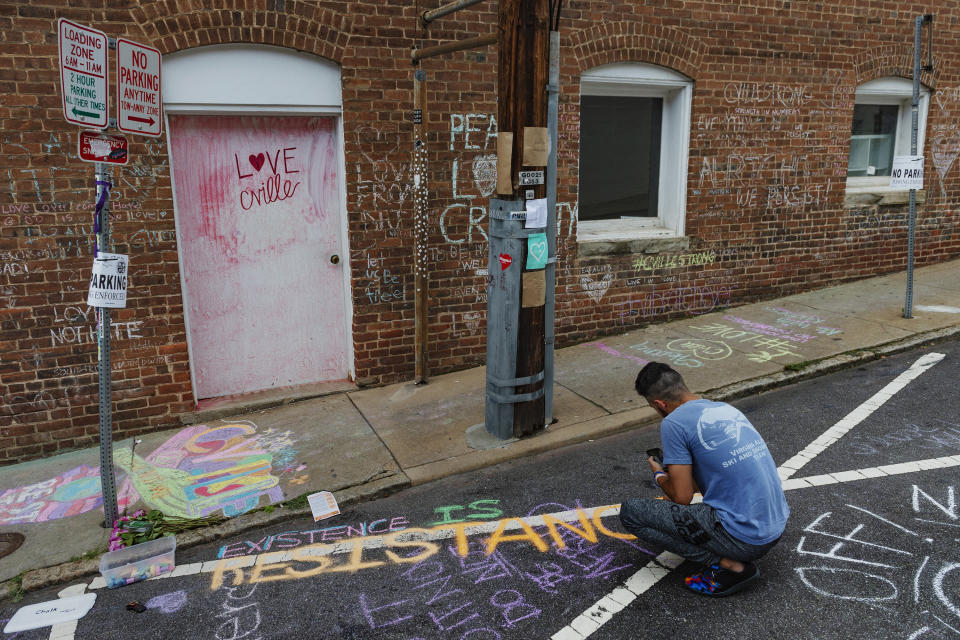 Ahmed Mohamed writes a message on the ground of the alleyway where a memorial for Heather Heyer who was killed during last year's Unite the Right rally, is located in Charlottesville, Va., Saturday, Aug. 11, 2018. The city of Charlottesville plans to mark Sunday's anniversary of a deadly gathering of white supremacists with a rally against racial hatred. (Craig Hudson/Charleston Gazette-Mail via AP)