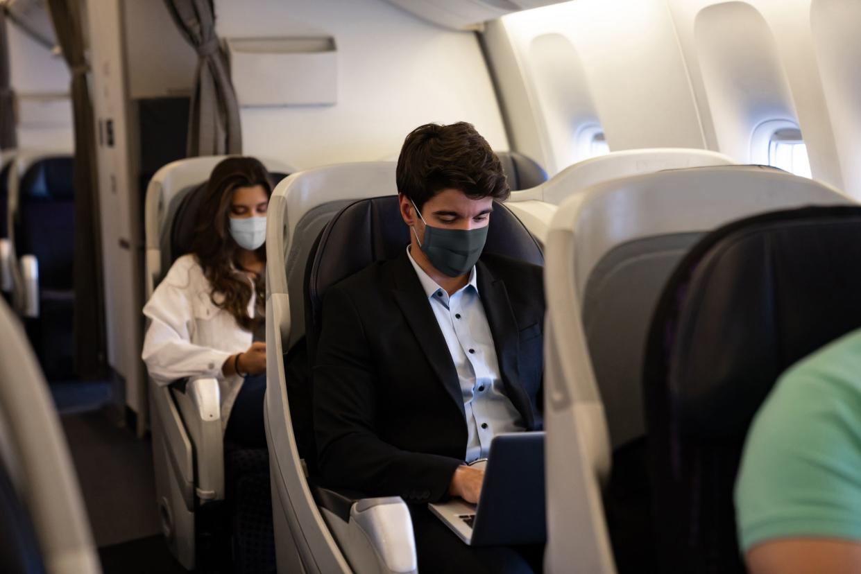 Business man traveling and wearing a facemask on the plane while using his laptopâ€“ COVID-19 pandemic lifestyle concepts