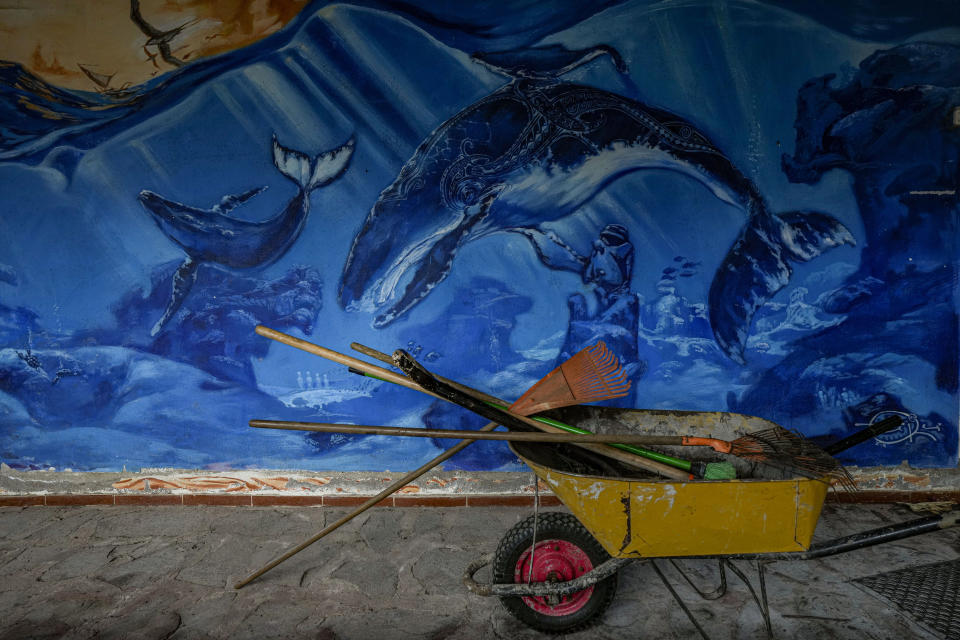 A wheelbarrow holding rakes and brooms sits by a mural depicting the sea, at a hotel under repairs in Hagan Roa, Rapa Nui, or Easter Island, Chile, Wednesday, Nov. 23, 2022. For two years there were no tourists, when the mayor banned foreigners from entering the island to protect the community from COVID-19. (AP Photo/Esteban Felix)