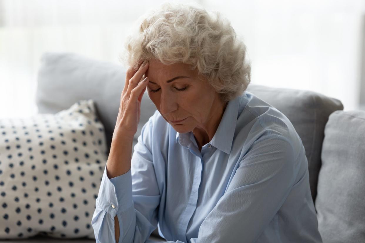 Sick senior woman sit on sofa at home feel distressed suffer from migraine or headache, ill mature female rest on couch touch head have dizziness from high blood pressure, elderly healthcare concept