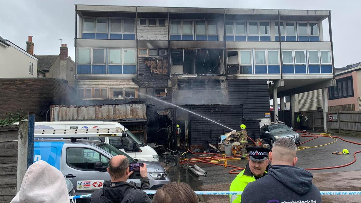 The multi-storey building in the background clearly damaged by fire, with people crowded in the foreground