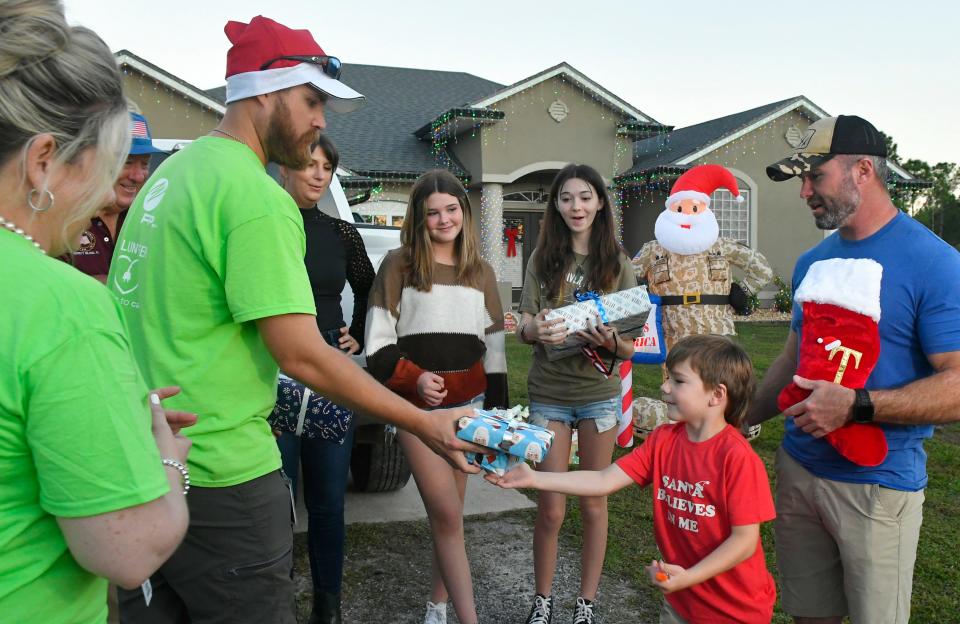 Case Trotter, 6, receives a gift from FPL volunteers. Florida Power & Light Company volunteers teamed up with the Military Order of the Purple Heart and the Brevard Veterans Memorial Center to surprise a U.S. Marine Corps veteran and his family with an energy-efficient holiday light display. Thomas Trotter, seen at far right in this photo, is a combat wounded veteran who served numerous tours, including Iraq and Afghanistan. He lives in Grant-Valkaria with his wife and three children.