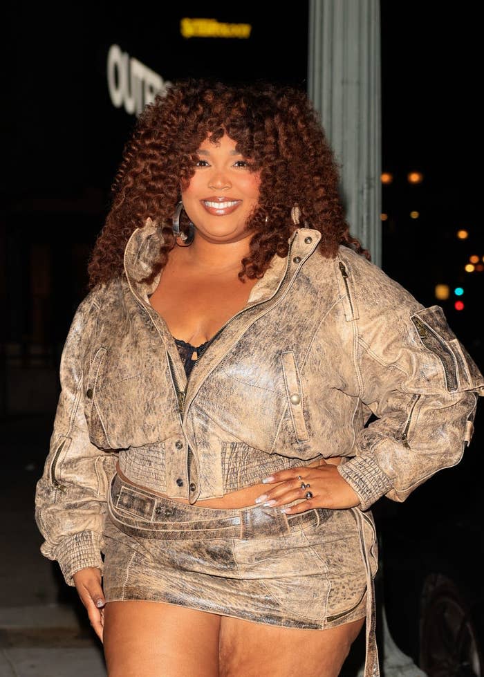 A woman with curly hair smiles while wearing a stylish structured jacket and matching skirt on an evening outing