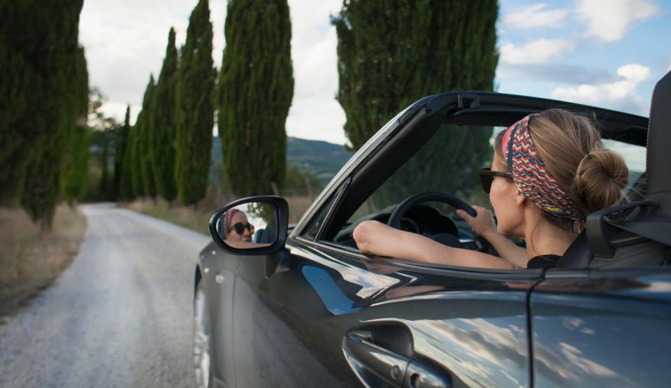 A stock image shows a woman driving a convertible car.
