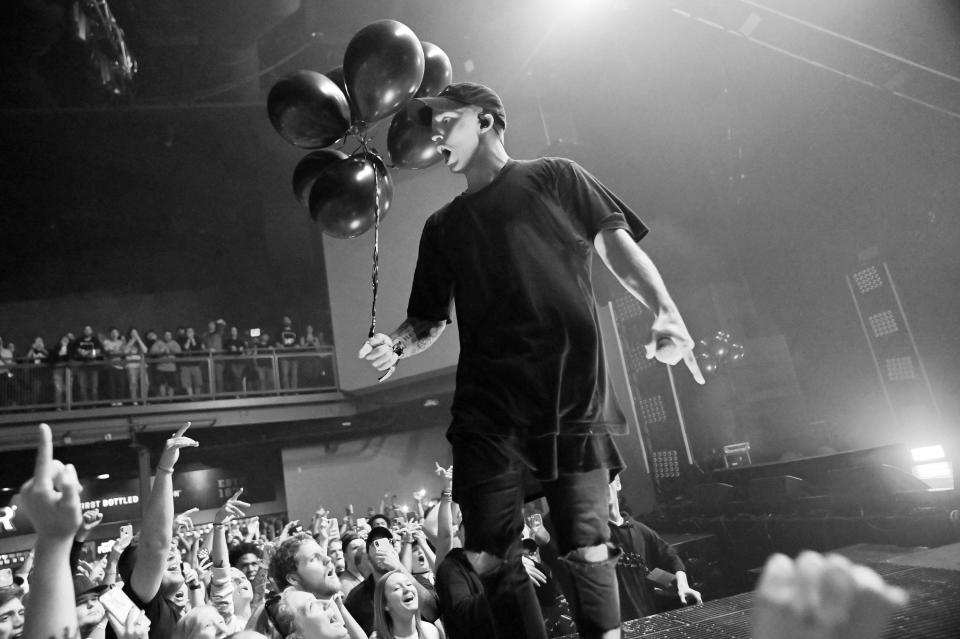 NF performs on stage while holding balloons in one hand.