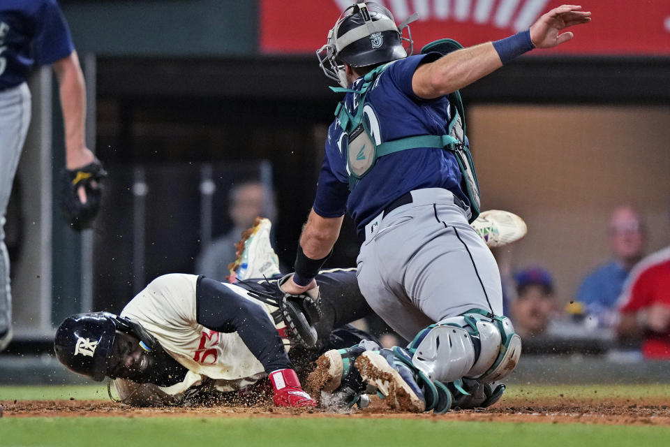 Texas Rangers' Adolis Garcia scores past Seattle Mariners catcher Cal Raleigh (29) during the fifth inning of a baseball game in Arlington, Texas, Friday, Sept. 22, 2023. (AP Photo/LM Otero)