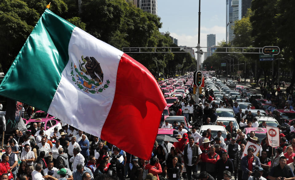 A Mexican national flag is waved as hundreds of taxi drivers gather to protest ride apps, in Mexico City, Monday, Oct. 7, 2019. The protesters want the apps banned, arguing that the apps are unfair competition because those drivers are more loosely regulated and don't have to pay licensing fees. (AP Photo/Marco Ugarte)