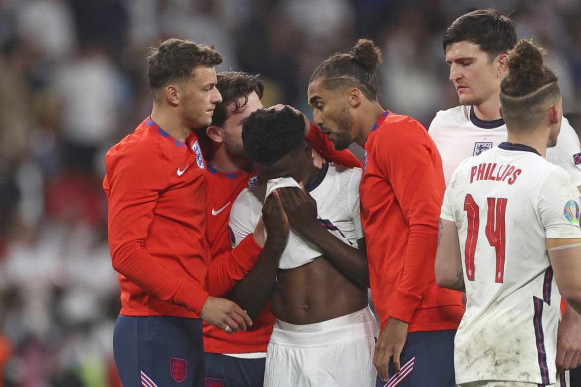 FILE – England players comfort teammate Bukayo Saka after he failed to score a penalty during a penalty shootout after extra time during of the Euro 2020 soccer championship final match between England and Italy at Wembley stadium in London, Sunday, July 11, 2021. Missing penalties in a major international soccer final was bad enough for three Black players, Marcus Rashford, Jadon Sancho and Bukayo Saka, who were on England’s national team. Being subjected to a torrent of racial abuse on social media in the aftermath made it even worse. Saka, who has more than 1 million followers on Twitter, remains on social media despite the abuse after England’s Euro 2020 loss. (Carl Recine/Pool Photo via AP, File)