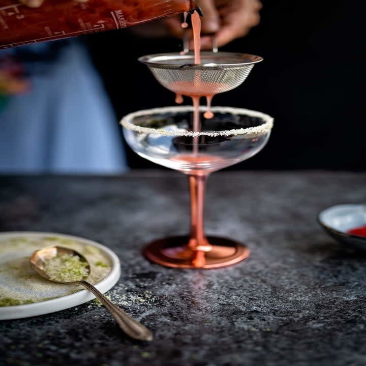 Pouring a strawberry gin cocktail into a coupe glass