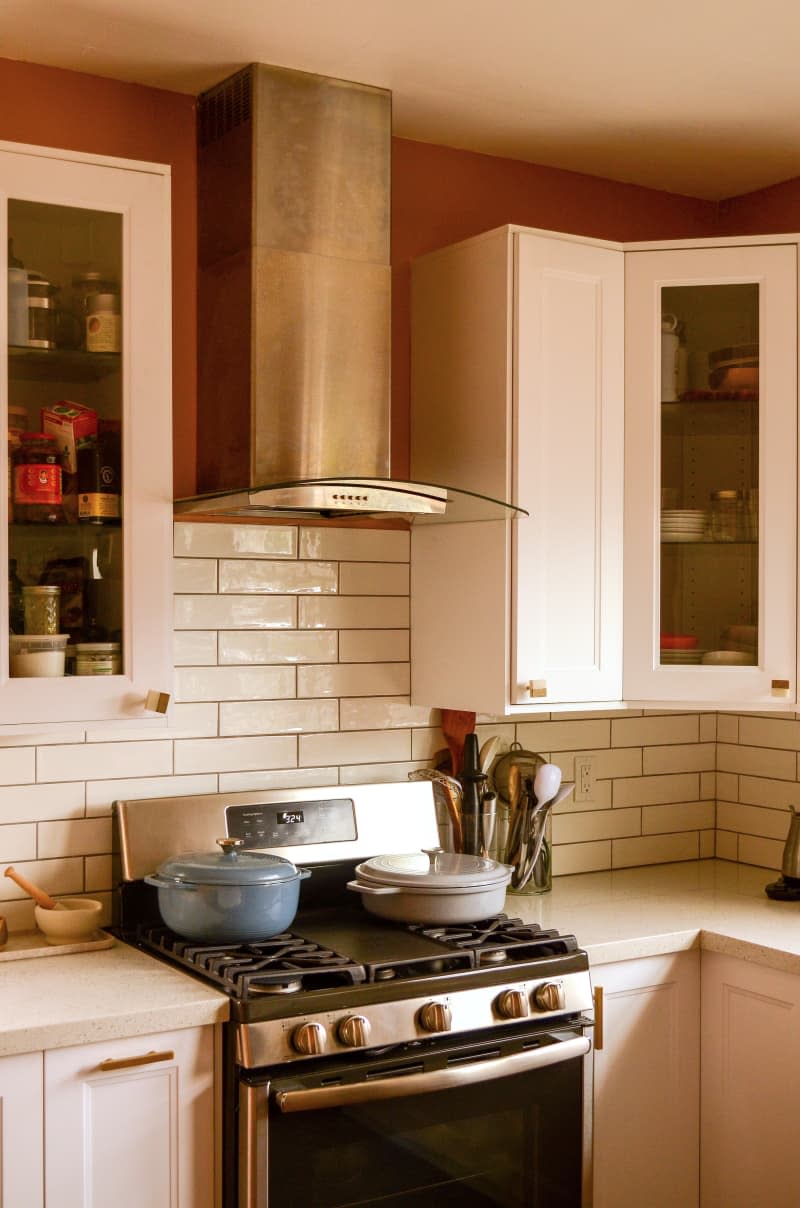 Oven and vent seen in kitchen with white subway tile.