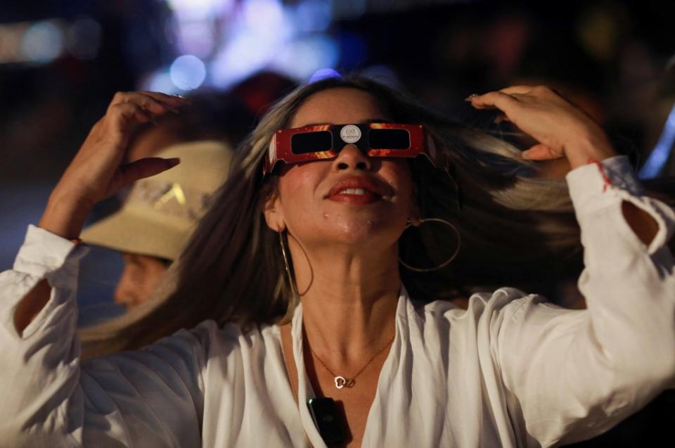 A woman demonstrating how to use special protective glasses for viewing the solar eclipse to tourists and residents at the Malecon in Mazatlan, Mexico. REUTERS