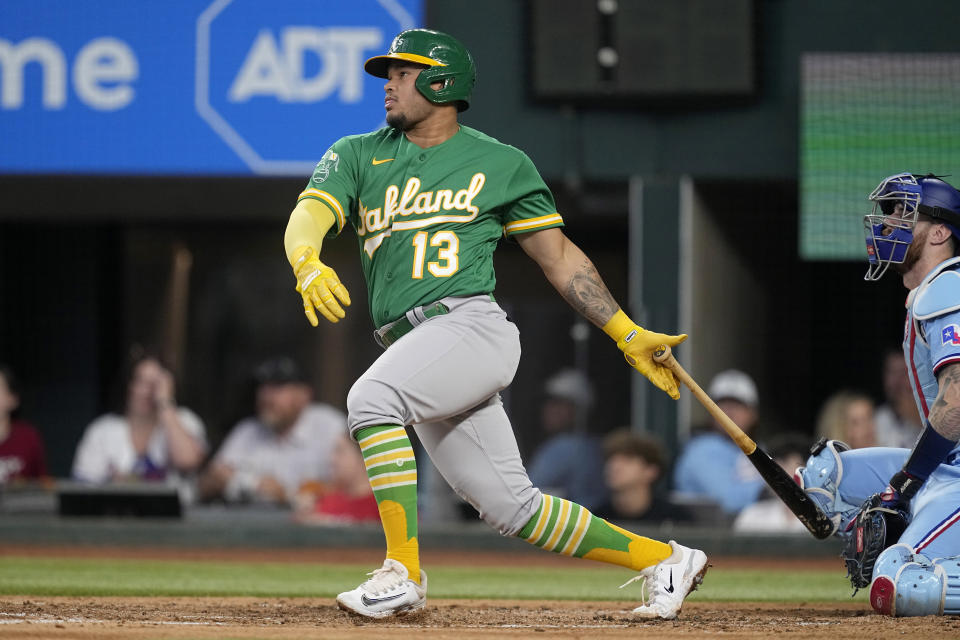 Oakland Athletics' Jordan Diaz (13) follows through on a run-scoring single as Texas Rangers' Jonah Heim, right, looks on in the third inning of a baseball game, Sunday, Sept. 10, 2023, in Arlington, Texas. Ryan Noda scored on the hit. (AP Photo/Tony Gutierrez)