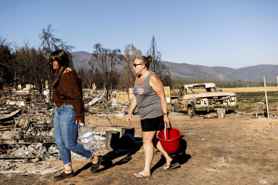 Kimberly Price and granddaughter Kyra Cedillos, 14, walk among burned homes in the Greenville community of Plumas County, Calif., on Sunday, Sept. 5, 2021, while feeding cats left behind by Dixie Fire evacuees. (AP Photo/Noah Berger)