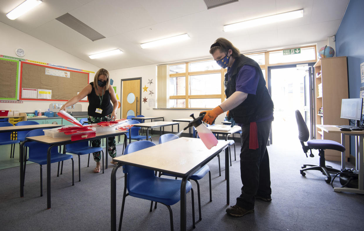 Joshua Lee, right, disinfects tables at Queen's Hill Primary School in Costessey near Norwich, England,  Monday, Aug. 24, 2020. Britain’s prime minister is asking parents to set aside their fears and send their children back to school next month when the nation’s schools fully reopen for the first time since the coronavirus pandemic shut then down more than five months ago. (Joe Giddens/PA via AP)