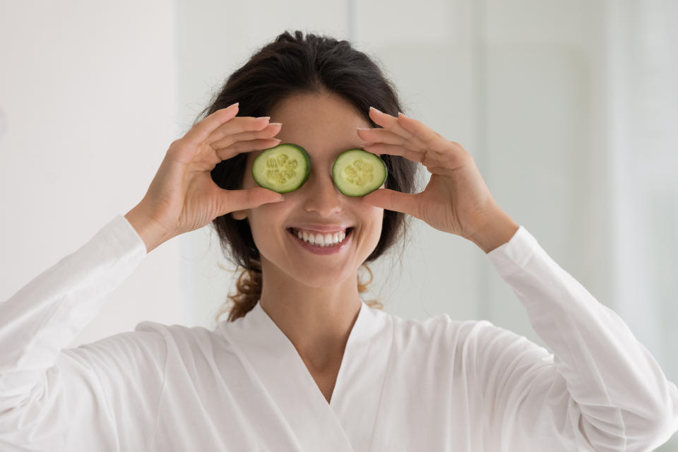 Smiling sincere millennial latina woman holding cucumber slices on eyes, feeling excited of anti wrinkles procedure, doing morning spa domestic skincare routine or recommending organic cosmetics use.