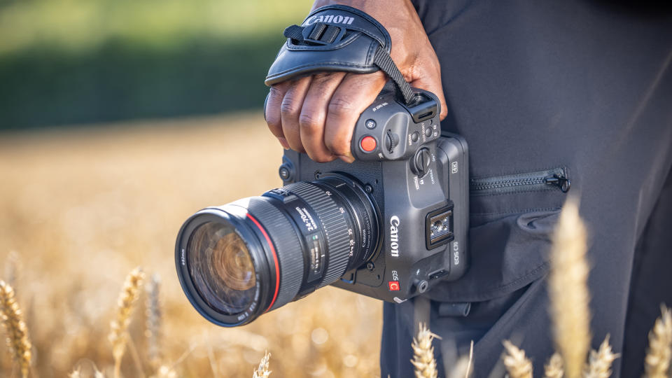 A man in a field holding a Canon EOS C70