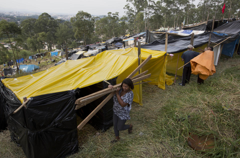 A woman carries wooden slats to build a shack on occupied land within view of Itaquerao stadium in Sao Paulo, Brazil, Tuesday, May 6, 2014. Thousands of impoverished Brazilians have squatted near the World Cup stadium hosting the opening match of soccer’s biggest tournament, saying the arena’s construction is to blame for rent increases that drove them out of their homes. (AP Photo/Andre Penner)