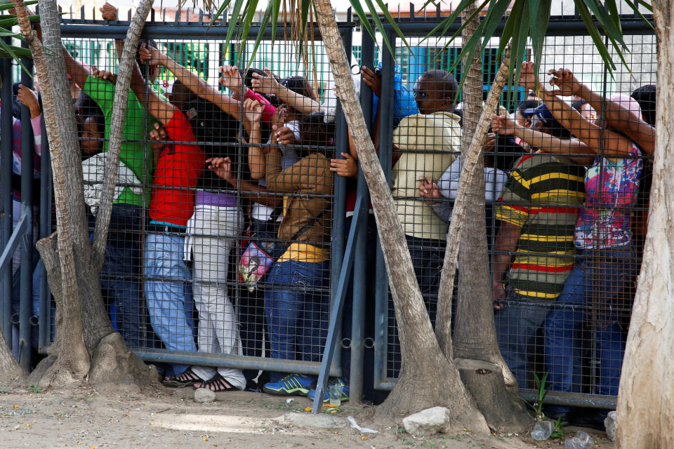 People queue next to a fence to try to buy food and staple items outside a supermarket in Caracas on May 17, 2016.