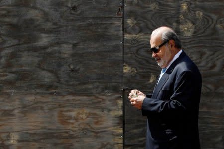 Mexican billionaire Carlos Slim holds money as he walks on a street after attending a ceremony to place the first stone of the new U.S. Embassy, in Mexico City, Mexico, February 13, 2018. REUTERS/Edgard Garrido